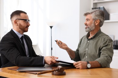 Man having meeting with professional lawyer at wooden desk indoors