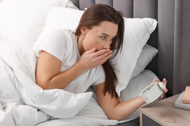 Overslept woman with alarm clock in bed at home