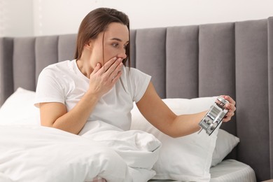 Overslept woman with alarm clock in bed at home