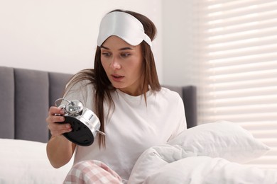 Overslept woman with alarm clock in bed at home