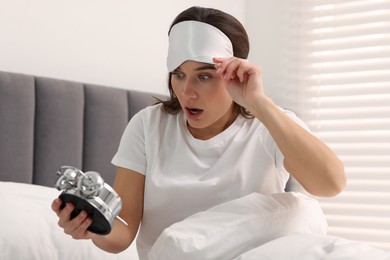 Overslept woman with alarm clock in bed at home