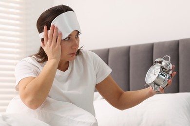 Overslept woman with alarm clock in bed at home