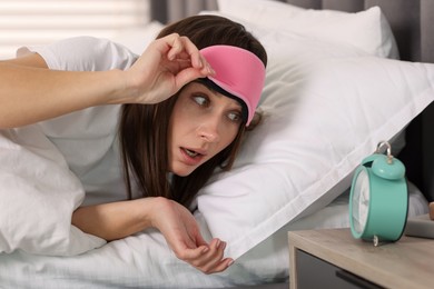 Overslept woman with alarm clock in bed at home