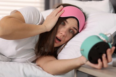 Overslept woman with alarm clock in bed at home