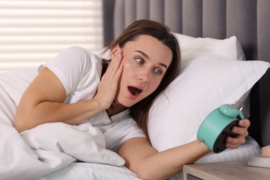 Overslept woman with alarm clock in bed at home