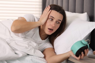 Overslept woman with alarm clock in bed at home