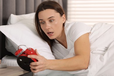 Photo of Overslept woman with alarm clock in bed at home