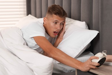 Photo of Overslept man with alarm clock in bed at home