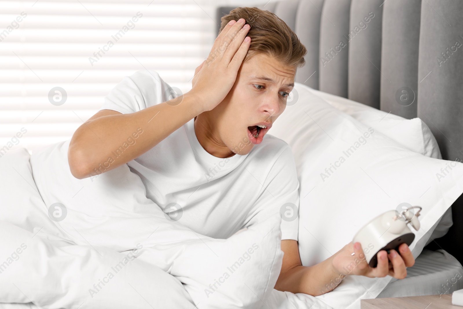 Photo of Overslept man with alarm clock in bed at home