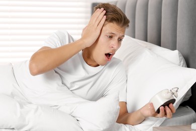 Photo of Overslept man with alarm clock in bed at home