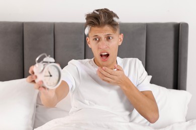 Photo of Overslept man with alarm clock in bed at home