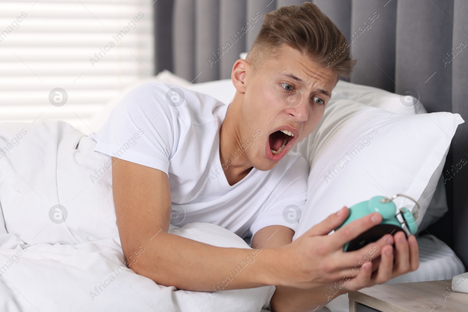 Photo of Overslept man with alarm clock in bed at home