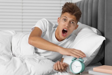 Photo of Overslept man with alarm clock in bed at home