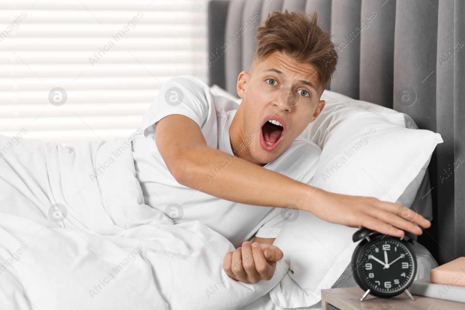 Photo of Overslept man with alarm clock in bed at home