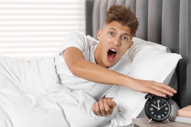 Photo of Overslept man with alarm clock in bed at home