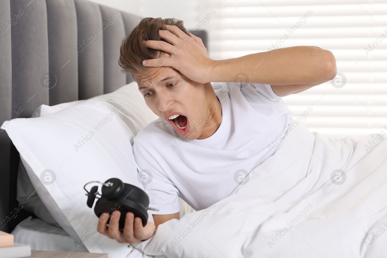 Photo of Overslept man with alarm clock in bed at home