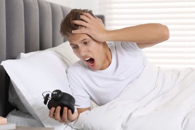 Photo of Overslept man with alarm clock in bed at home