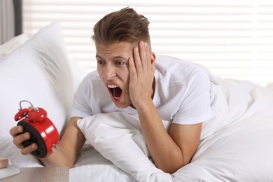 Photo of Overslept man with alarm clock in bed at home