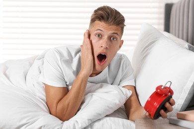 Photo of Overslept man with alarm clock in bed at home