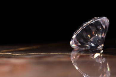 Photo of Beautiful shiny gemstone on brown marble surface against dark background, closeup. Space for text