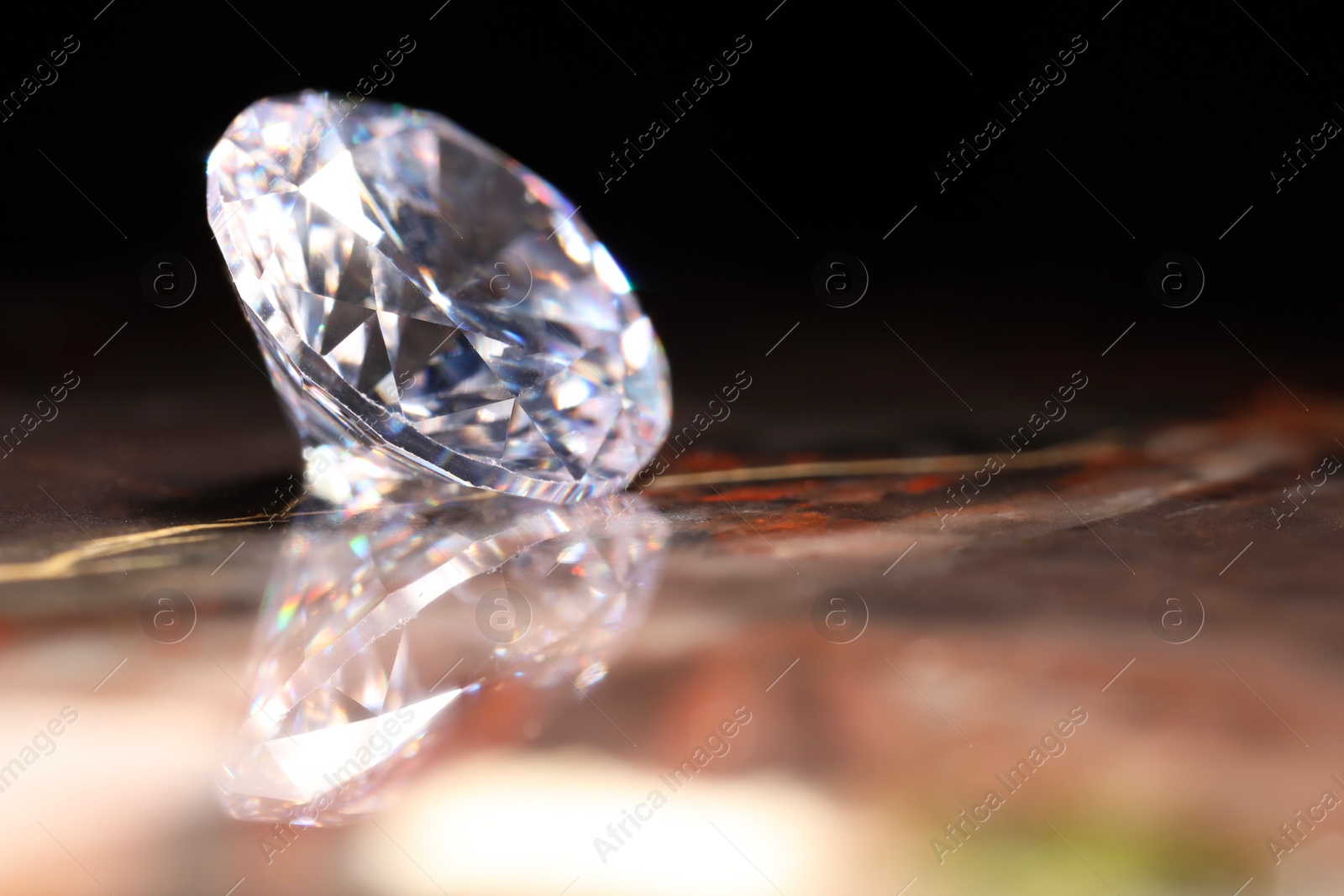 Photo of Beautiful shiny gemstone on brown marble surface against dark background, closeup. Space for text