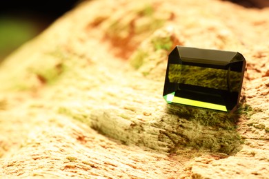 Photo of Beautiful shiny green gemstone on stone, space for text