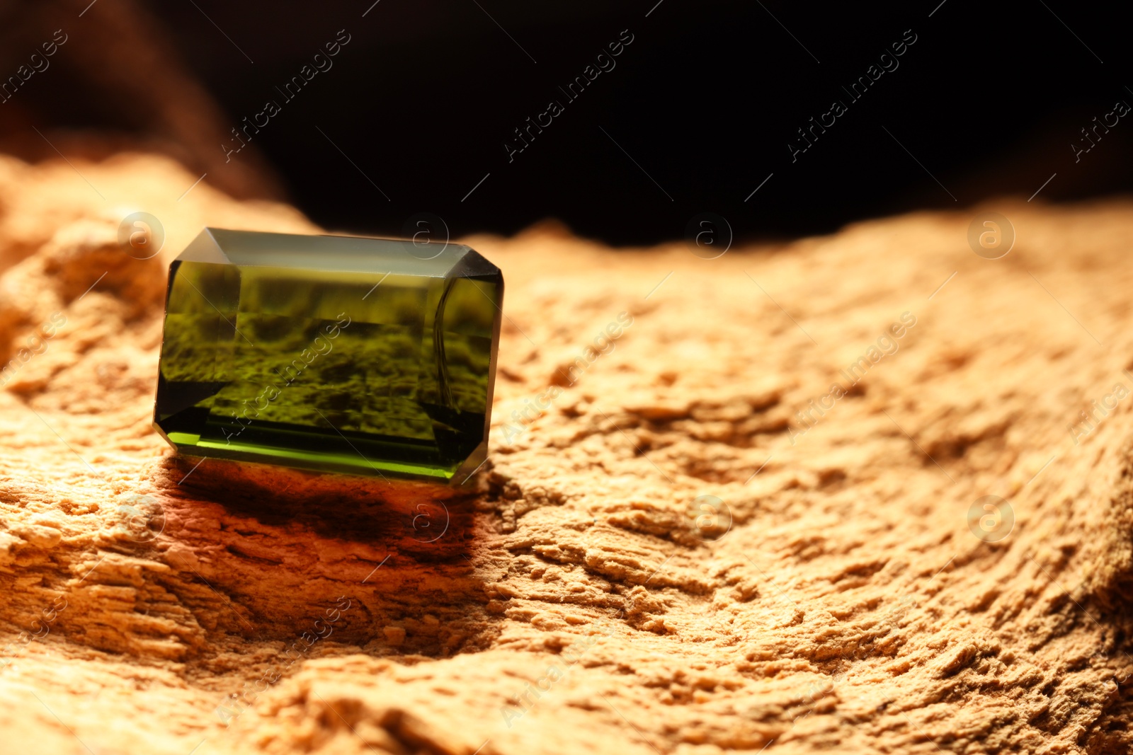 Photo of Beautiful shiny green gemstone on stone, space for text