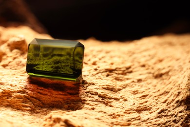 Photo of Beautiful shiny green gemstone on stone, space for text