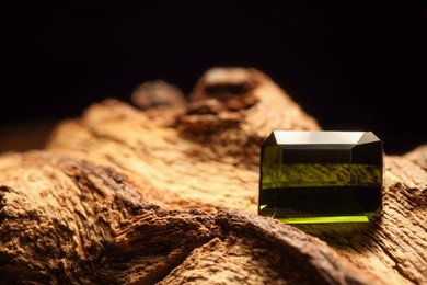 Photo of Beautiful shiny green gemstone on stone against dark background, space for text