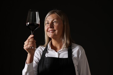 Photo of Professional sommelier analyzing quality of red wine on black background