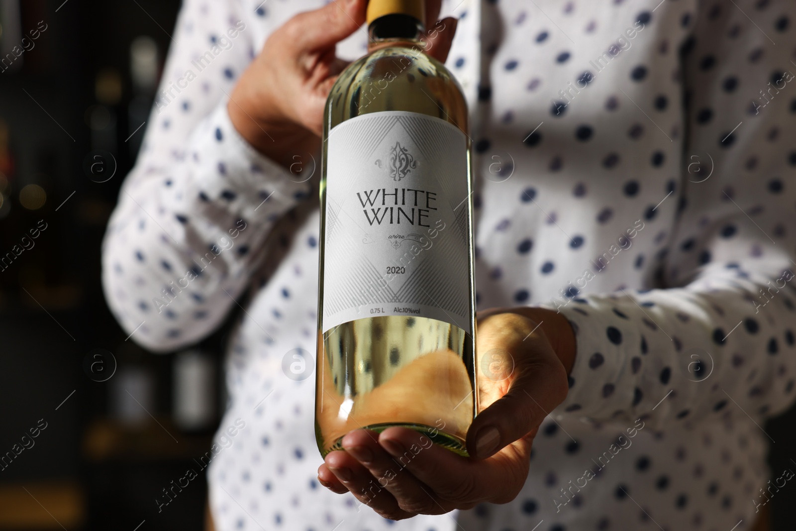 Photo of Professional sommelier holding bottle of white wine indoors, closeup