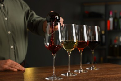 Photo of Professional sommelier pouring red wine into glasses on wooden table indoors, closeup