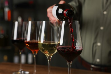 Photo of Professional sommelier pouring red wine into glasses on wooden table indoors, closeup