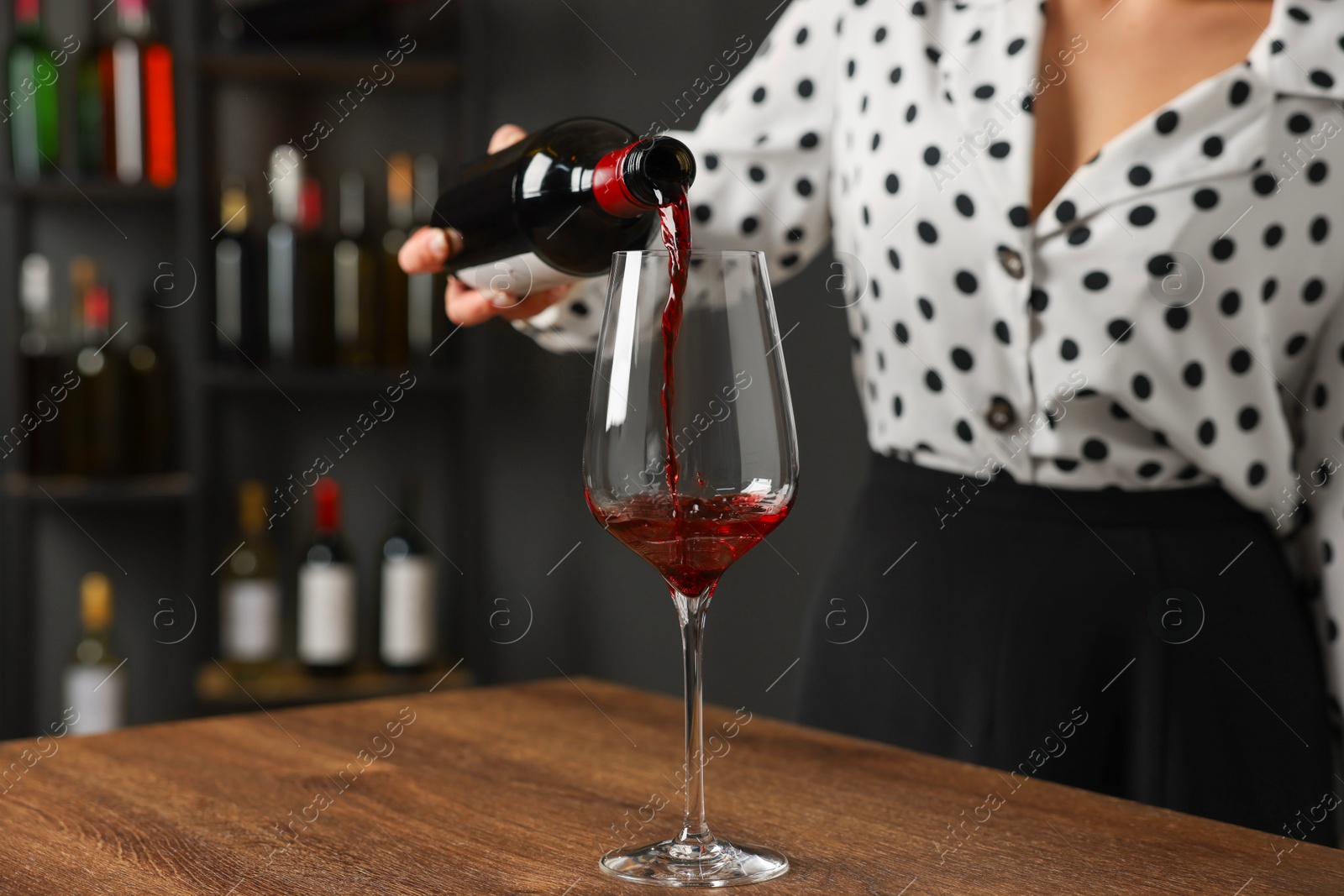 Photo of Professional sommelier pouring red wine into glass at wooden table indoors, closeup