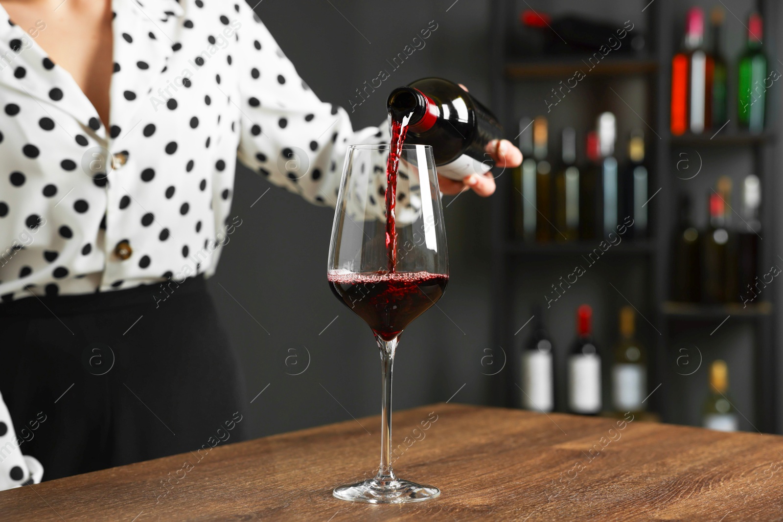 Photo of Professional sommelier pouring red wine into glass at wooden table indoors, closeup