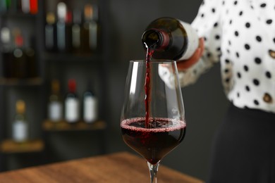 Photo of Professional sommelier pouring red wine into glass at wooden table indoors, closeup