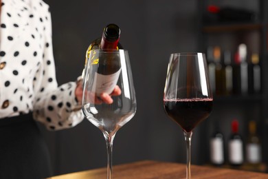 Photo of Professional sommelier pouring red wine into glasses at wooden table indoors, closeup