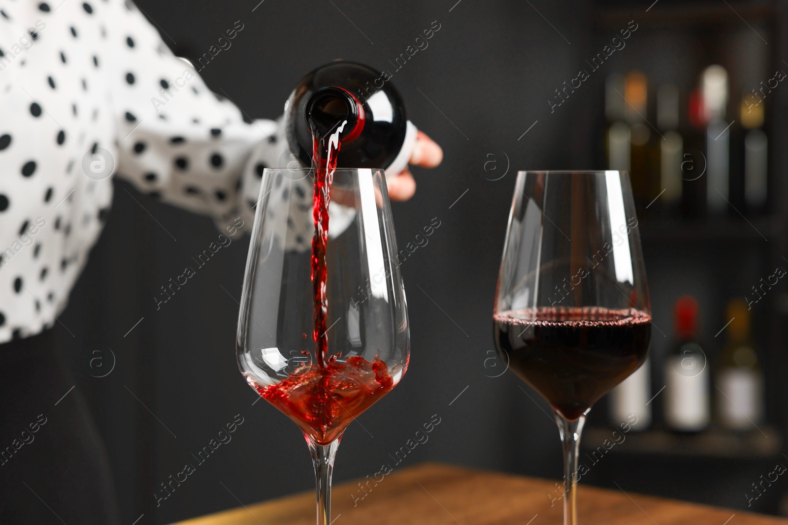 Photo of Professional sommelier pouring red wine into glasses at wooden table indoors, closeup