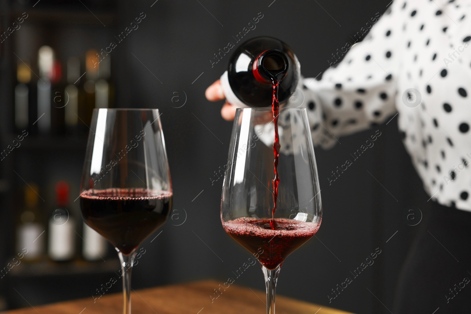 Photo of Professional sommelier pouring red wine into glasses at wooden table indoors, closeup