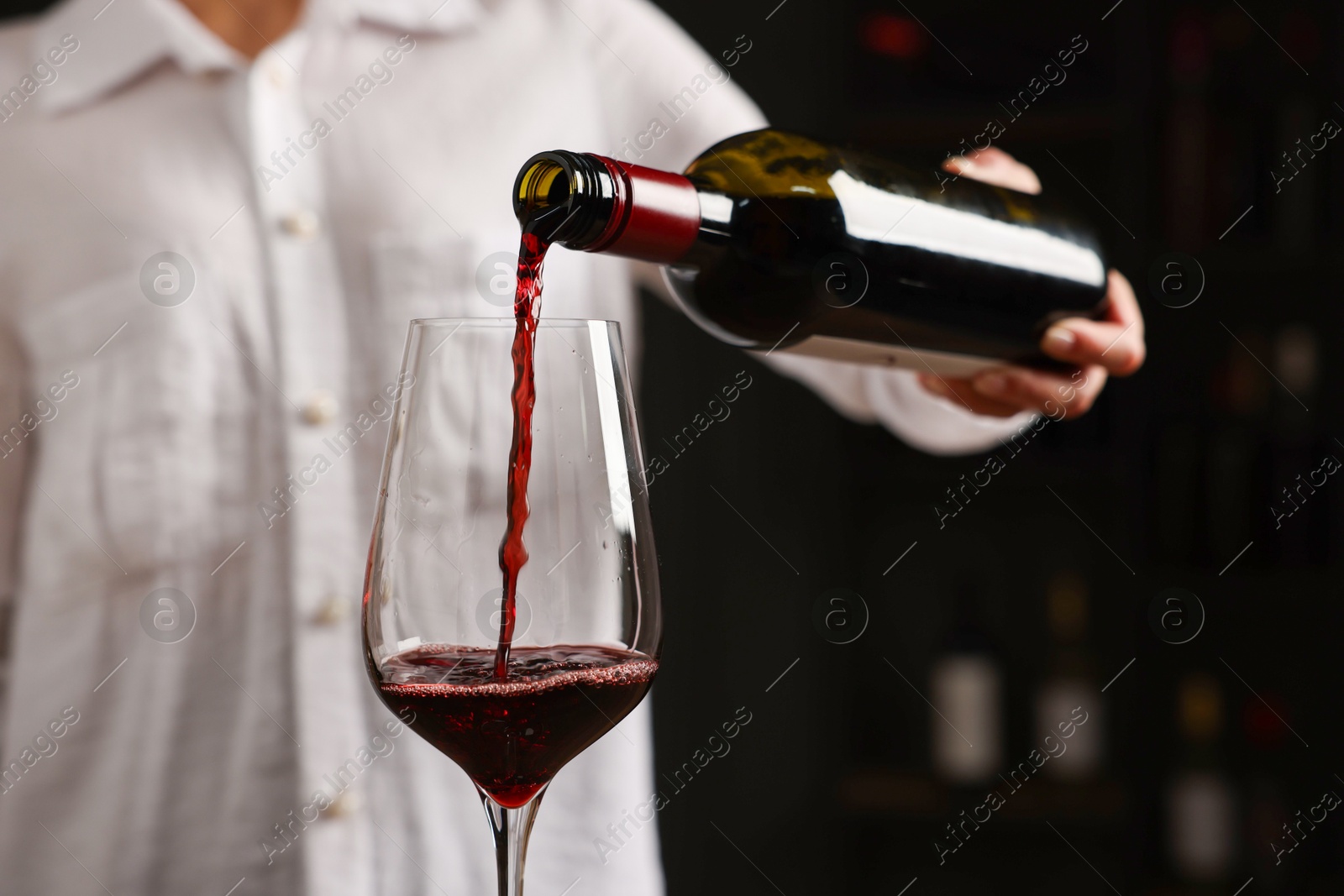 Photo of Professional sommelier pouring red wine into glass indoors, closeup