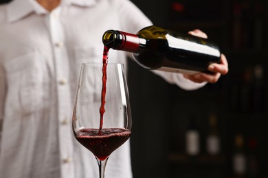 Photo of Professional sommelier pouring red wine into glass indoors, closeup