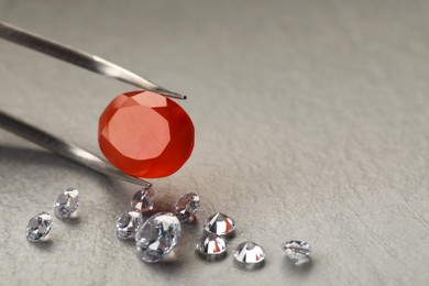 Photo of Tweezers with beautiful gemstones on textured table, closeup. Space for text