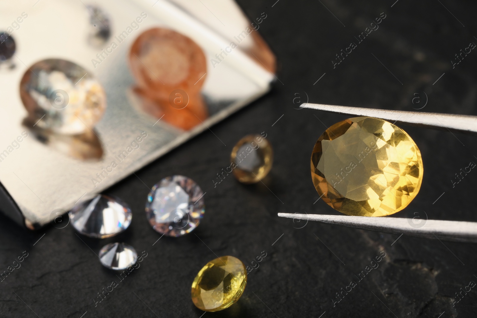 Photo of Tweezers with beautiful gemstones on black table, selective focus