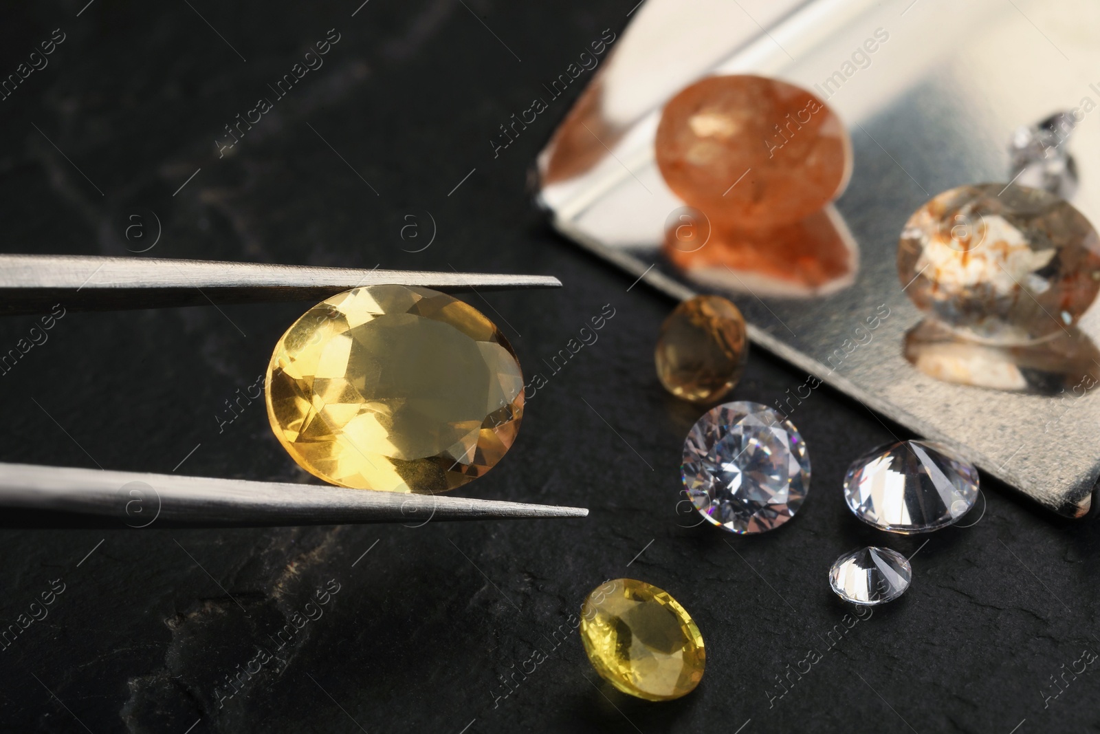 Photo of Tweezers with beautiful gemstones on black table, selective focus