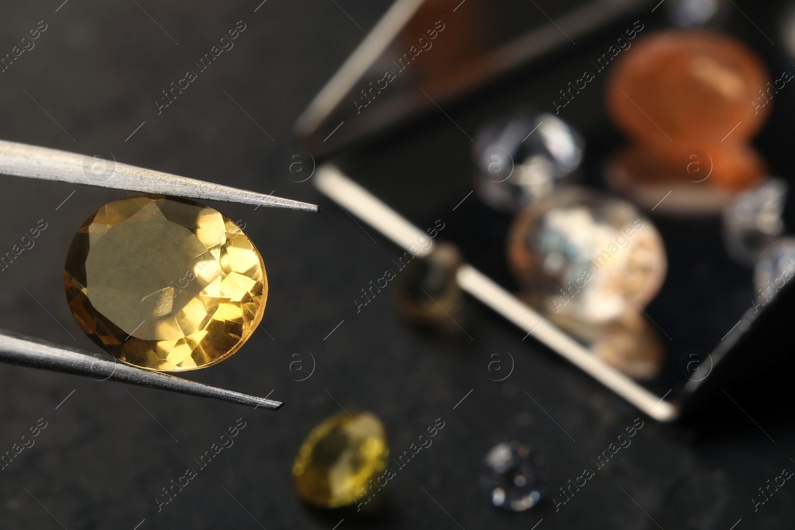 Photo of Tweezers with beautiful gemstone on blurred background, closeup