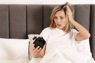 Photo of Overslept woman with alarm clock in bed at home