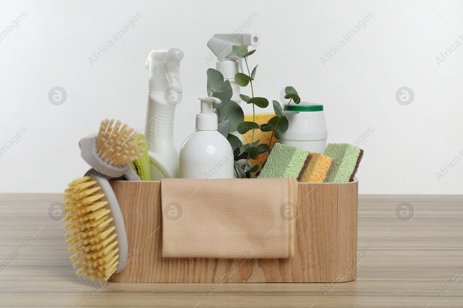 Photo of Eco-friendly cleaning products, supplies and eucalyptus branches in crate on wooden table