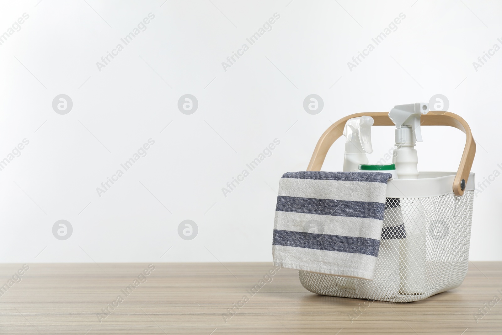 Photo of Different cleaning products and rag in basket on wooden table, space for text