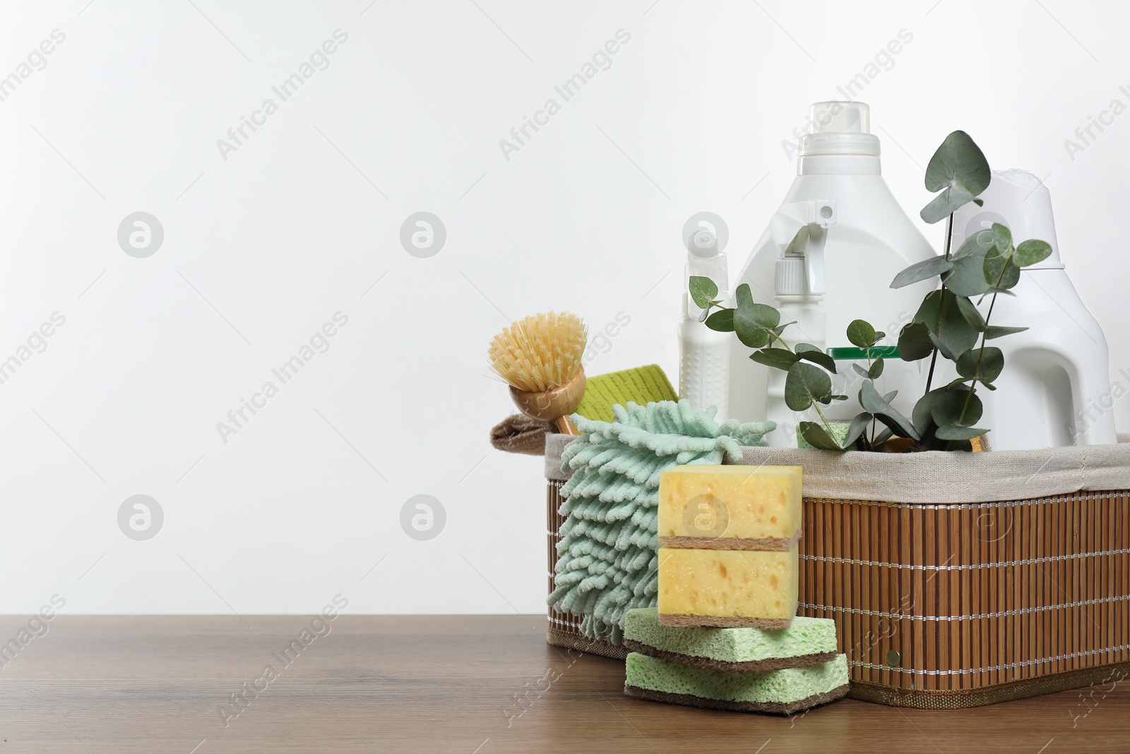 Photo of Eco-friendly cleaning products, supplies and eucalyptus branches in basket on wooden table, space for text