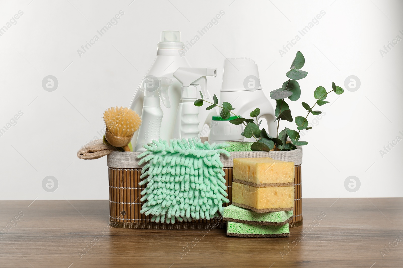 Photo of Eco-friendly cleaning products, supplies and eucalyptus branches in wicker basket on wooden table